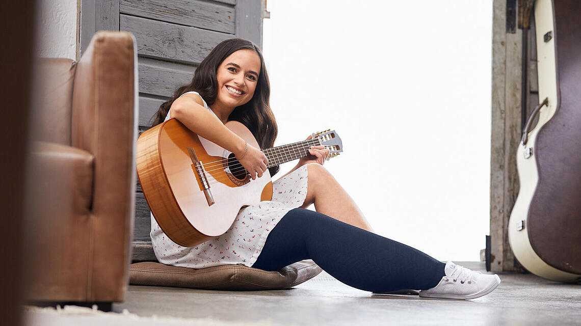 junge Frau mit einseitigem Beinödem und Kompressionsstrumpf spielt Gitarre, Foto:www.medi.de